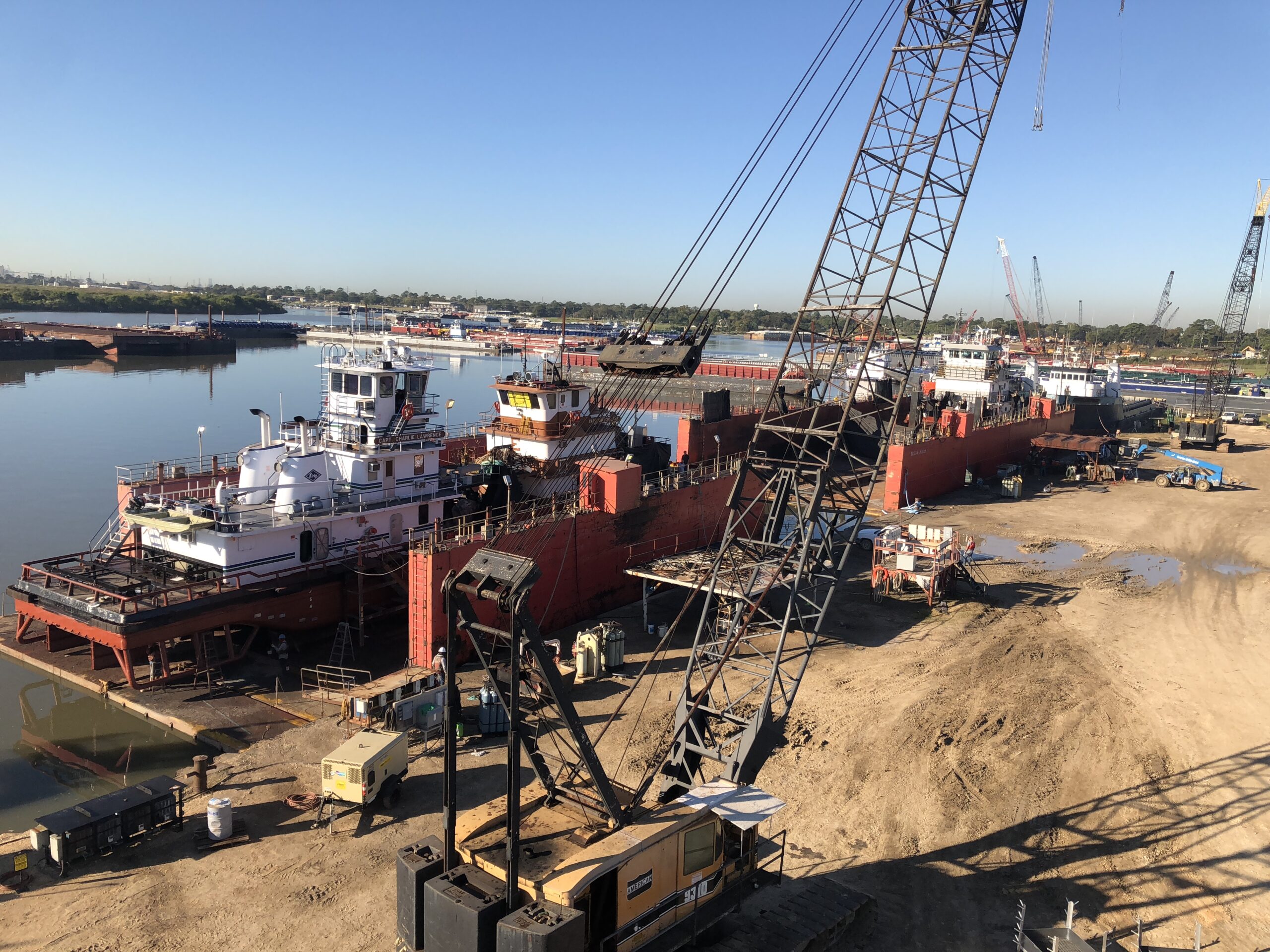 A crane is in the sand near some boats.